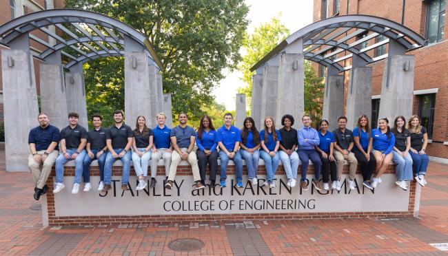 Group of Engineering Ambassadors sitting on Pigman College of Engineering sign in engineering courtyard